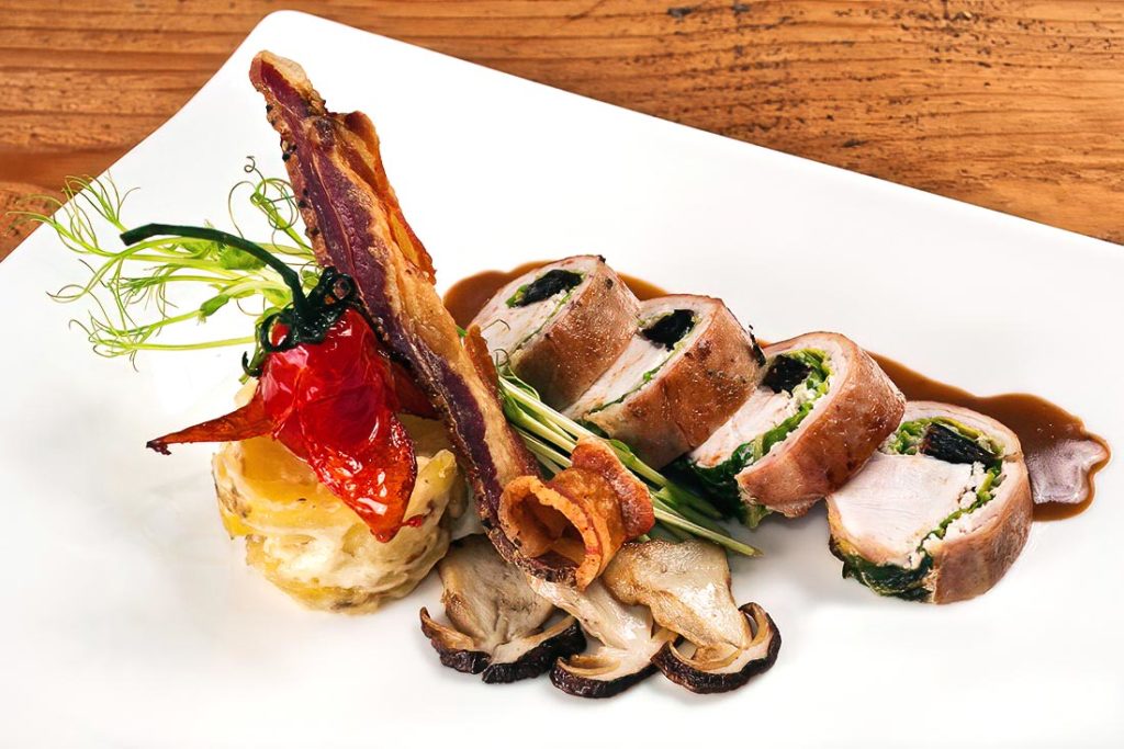 An exquisite gourmet dish featuring tender bacon-wrapped rabbit loins, earthy mushrooms, and roasted vegetables—perfect for special occasions.